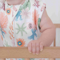 Baby wearing a colourful dreamy days floral dream swaddle holding onto a wooden crib rail.