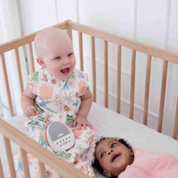 Two babies in a crib wearing the Dreamy Days dream swaddle with one wearing a pink coral and the other in pink together with the Dream pod white noise machine.