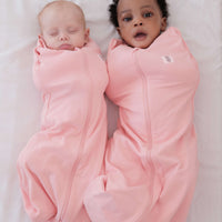 Two babies wrapped in dreamy days pink dream swaddles on a white surface