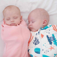 Two babies swaddled in pink and colourful ocean theme design dreamy days dream swaddle on a white background