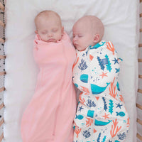 Two babies swaddled in pink and colourful ocean theme design dreamy days dream swaddle on a white background