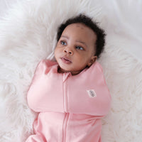 Baby in a dreamy days pink swaddle lying on a white fluffy surface