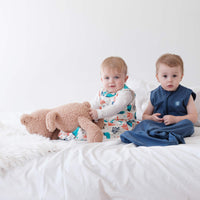 Two toddlers wearing the dreamy days navy and ocean themed dream sacks on white bed with a teddy bear