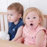 Two toddlers wearing the Dreamy days navy dream swaddle and the pink dream swaddle holding a dream pod white noise machine