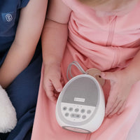 Two toddlers wearing the Dreamy days navy dream swaddle and the pink dream swaddle holding a dream pod white noise machine