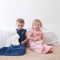 Two toddlers sitting by bed wearing the Dreamy days navy dream swaddle and the pin dream swaddle