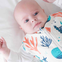 Newborn baby swaddled in a coluorful dreamy days dream swaddle with ocean-themed design, lying on a white surface.