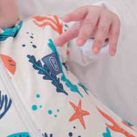 Newborn baby swaddled in a colourful dreamy days dream swaddle with ocean-themed design, lying on a white surface.