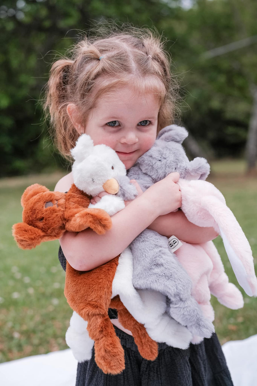 Child holding multiple Dreamy Days animal comforters outdoors
