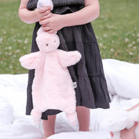Child in a dark dress holding a pink bunny comforter on a grassy area.