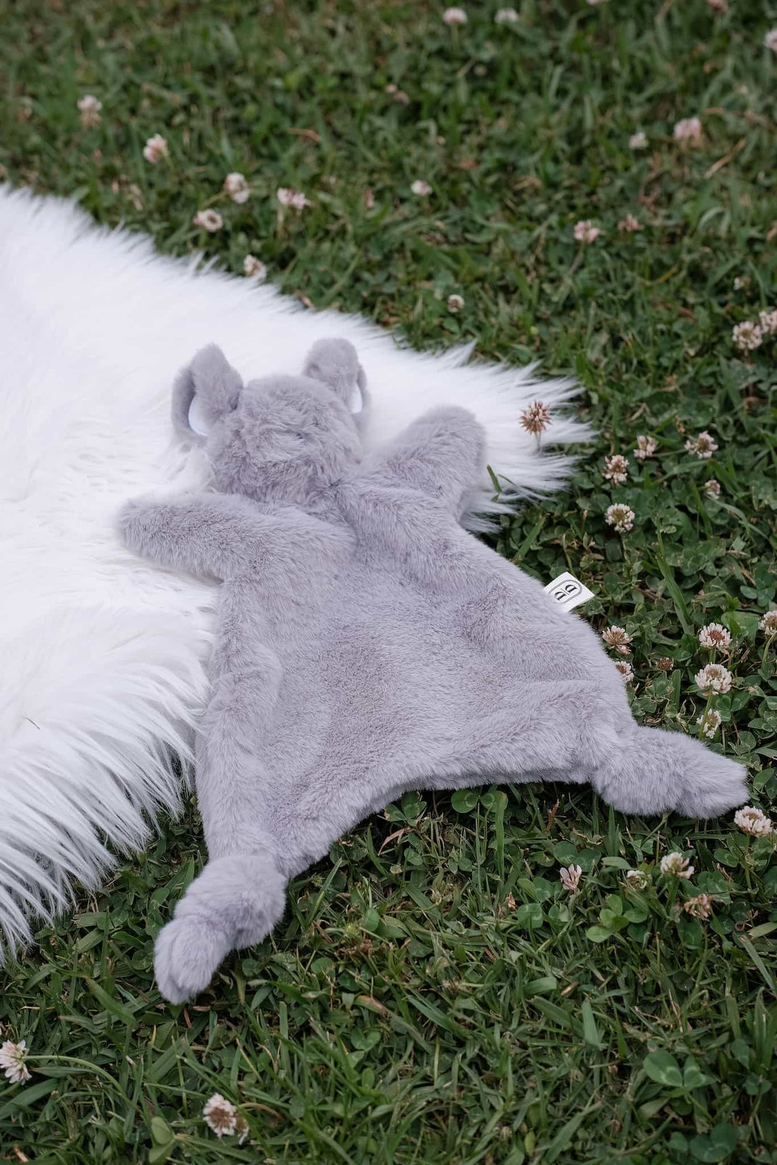 Dreamy Days Grey mouse plush toy on a white fur rug lying on grass.