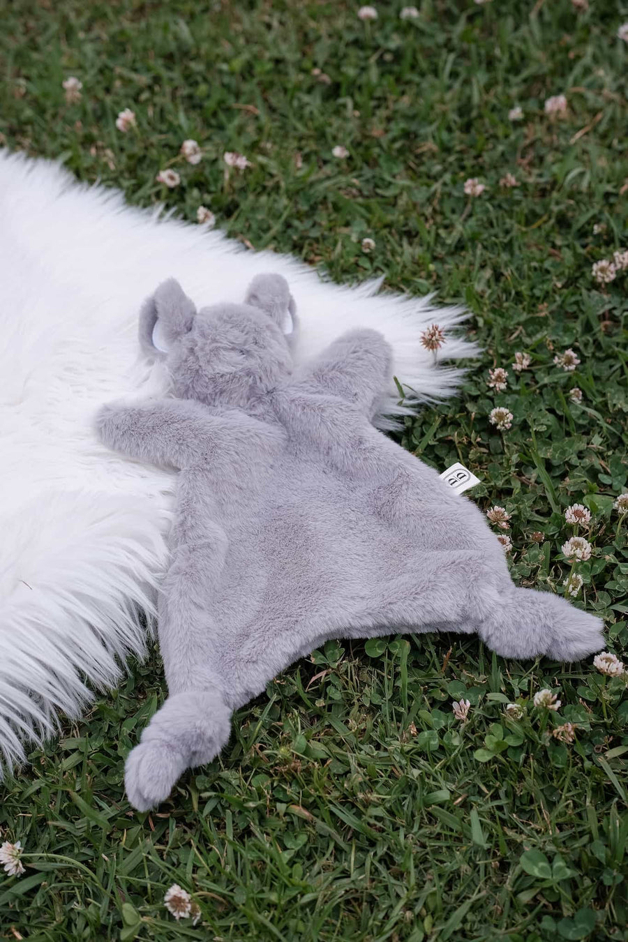 Dreamy Days Grey mouse plush toy on a white fur rug lying on grass.