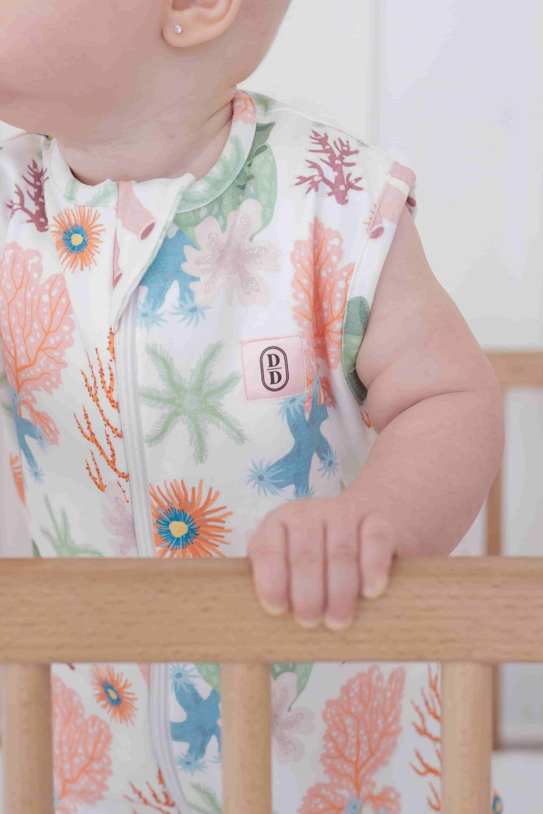 Baby wearing a colourful dreamy days floral dream swaddle holding onto a wooden crib rail.