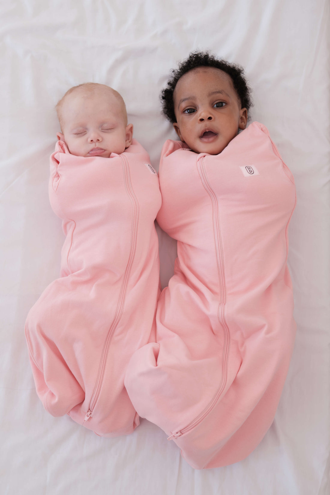 Two babies wrapped in dreamy days pink dream swaddles on a white surface