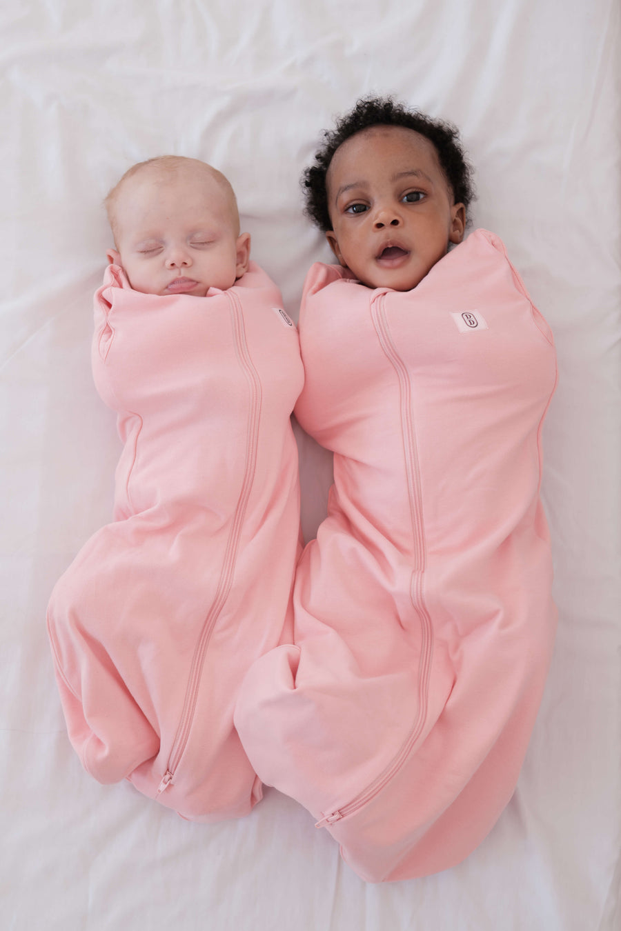 Two babies wrapped in dreamy days pink dream swaddles on a white surface