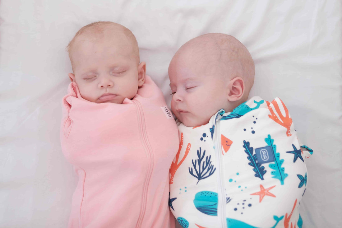 Two babies swaddled in pink and colourful ocean theme design dreamy days dream swaddle on a white background