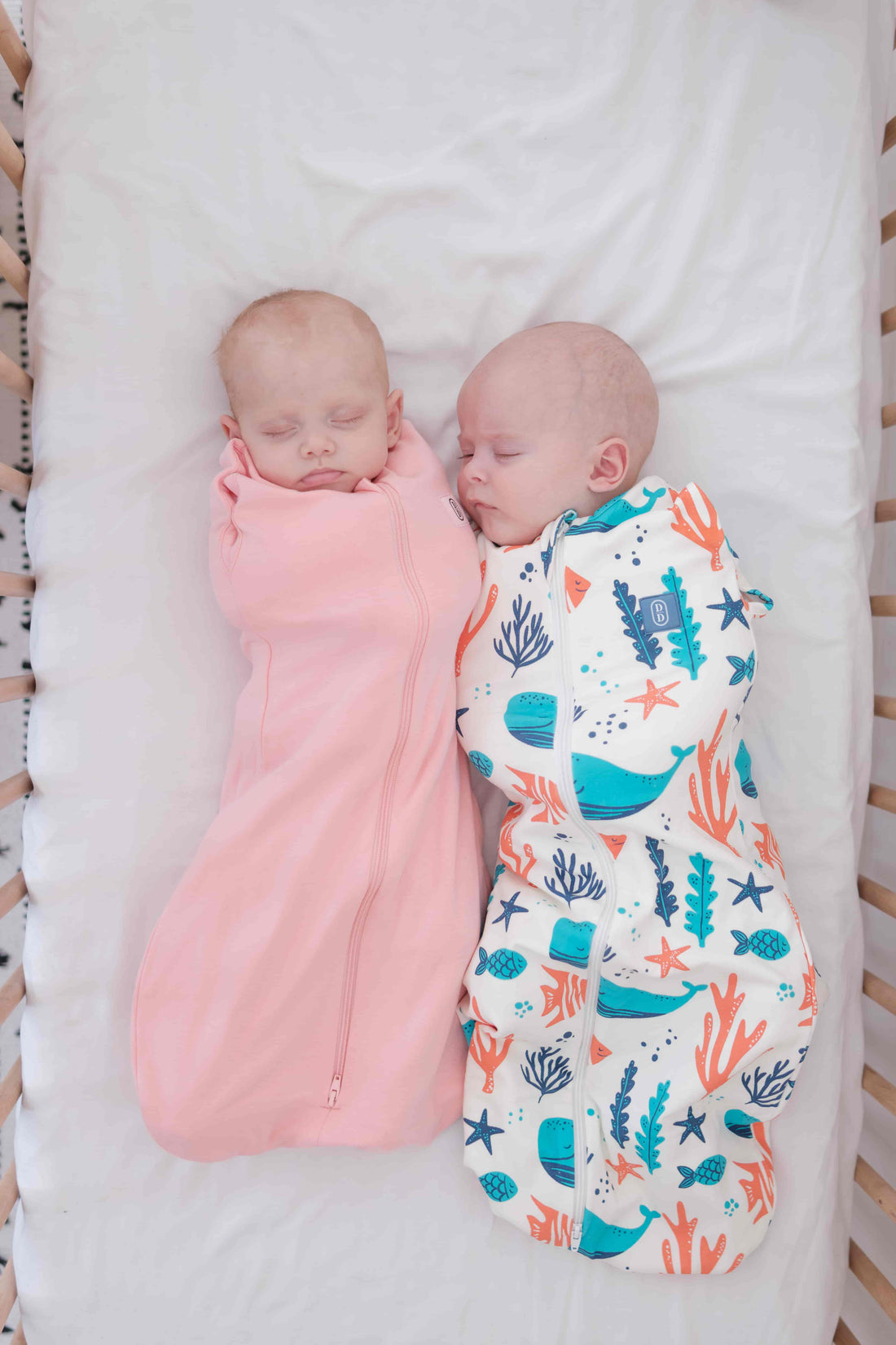Two babies swaddled in pink and colourful ocean theme design dreamy days dream swaddle on a white background