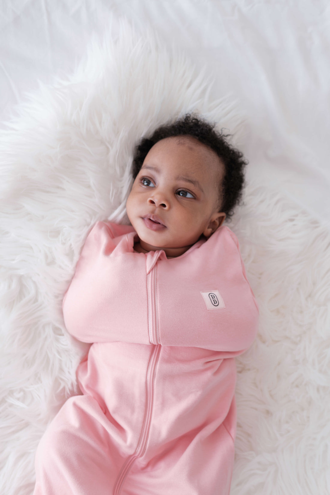 Baby in a dreamy days pink swaddle lying on a white fluffy surface