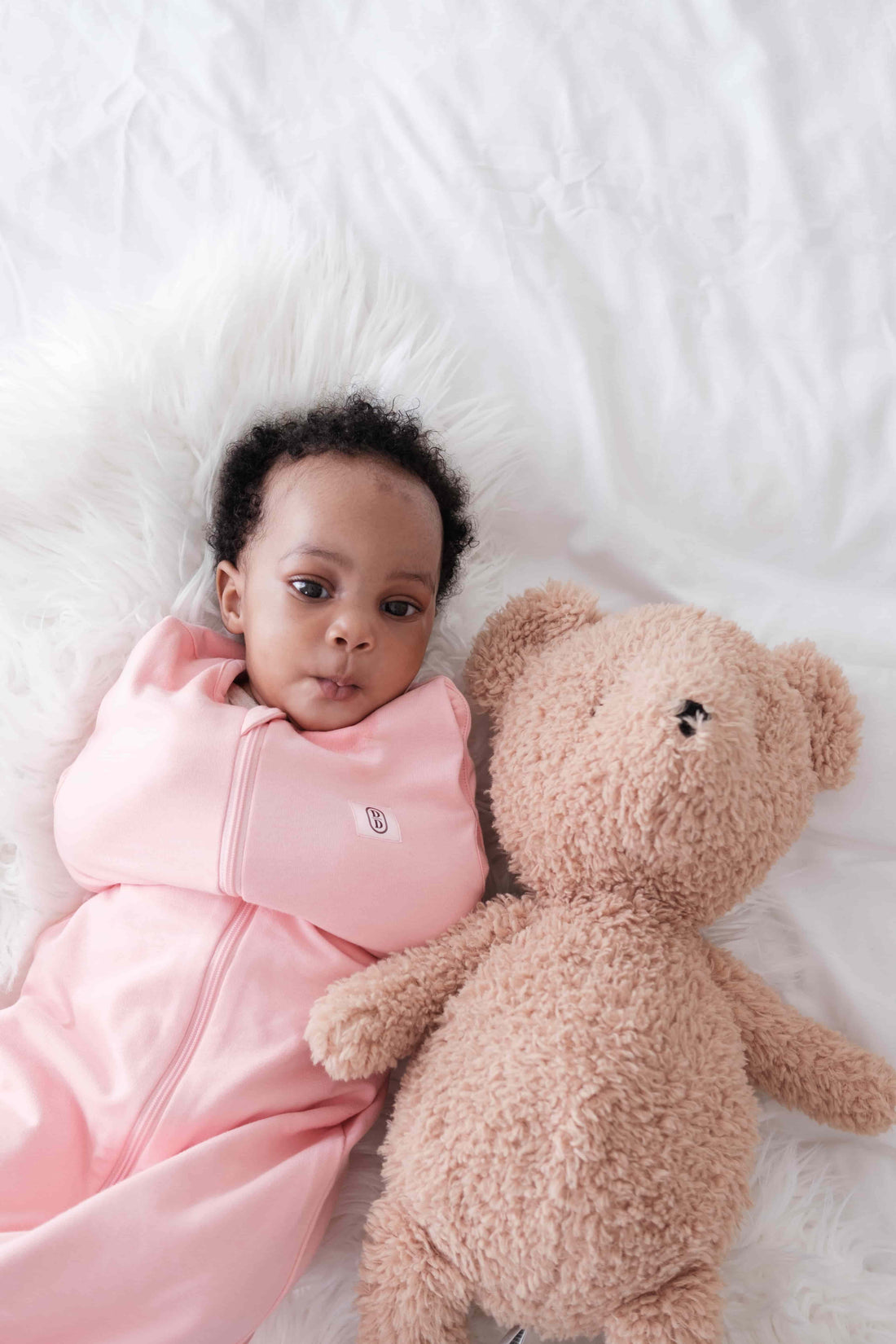 Baby wearing dreamy days pink dream swaddle lying next to brown bear
