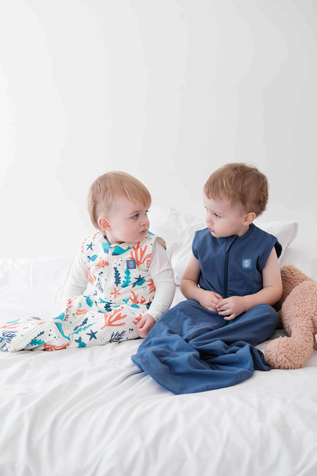 Two Baby and toddler wearing the Dreamy Days navy and ocean themed dream sack on white bed