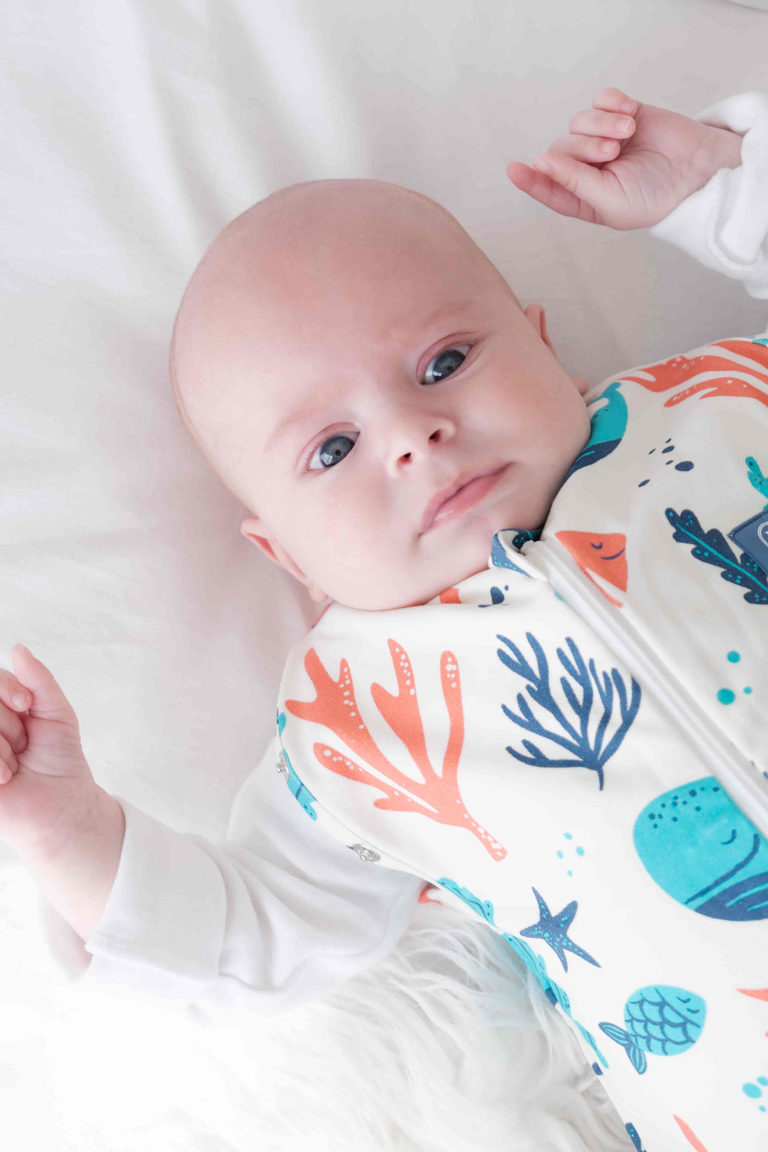 Newborn baby swaddled in a coluorful dreamy days dream swaddle with ocean-themed design, lying on a white surface.