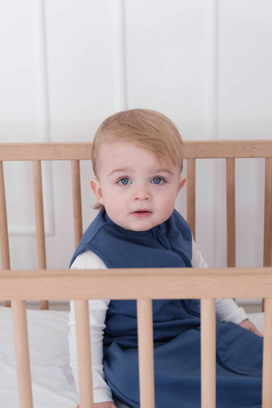 Toddler wearing a dreamy days navy dream sack in cot with white background