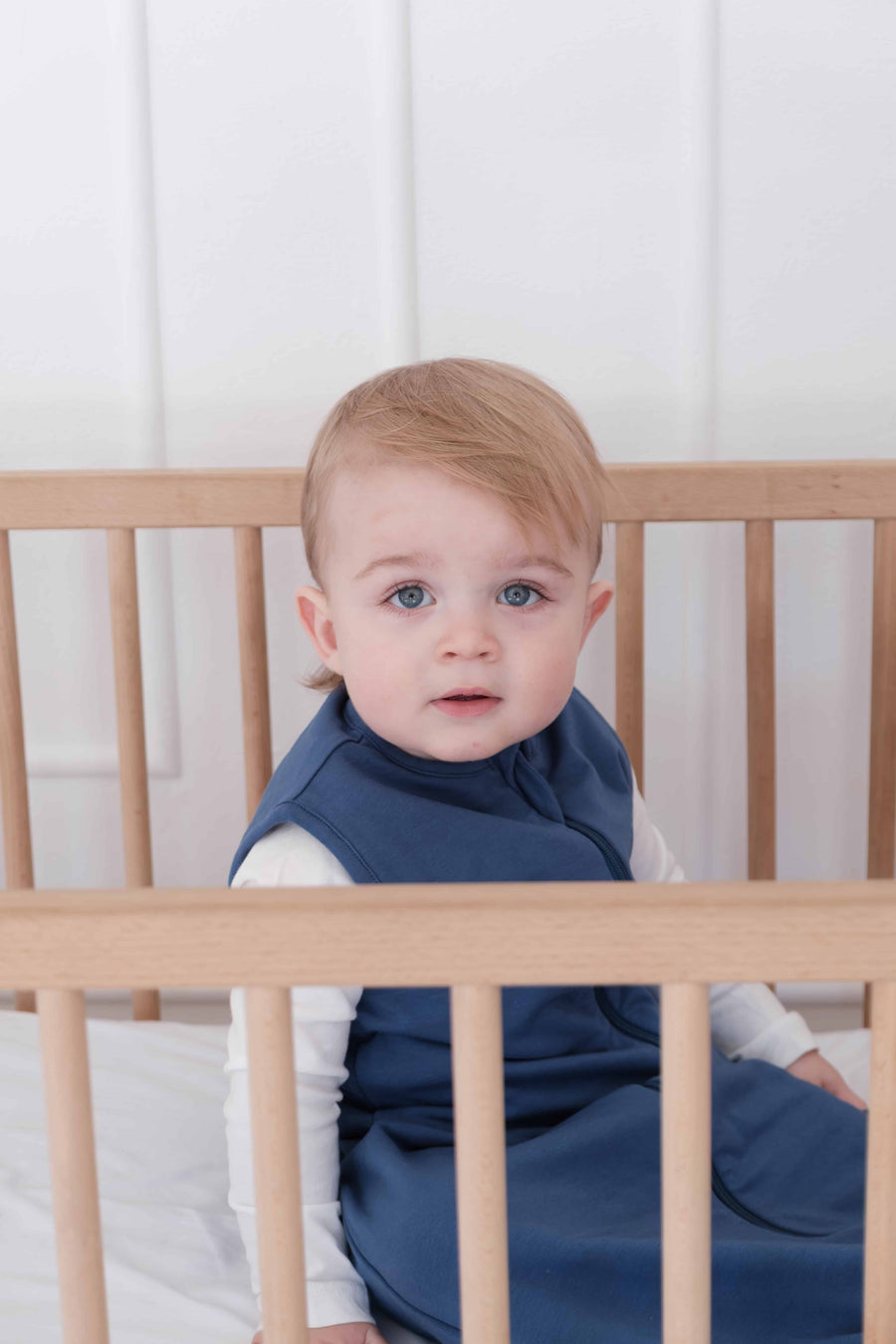 Toddler wearing a dreamy days navy dream sack in cot with white background