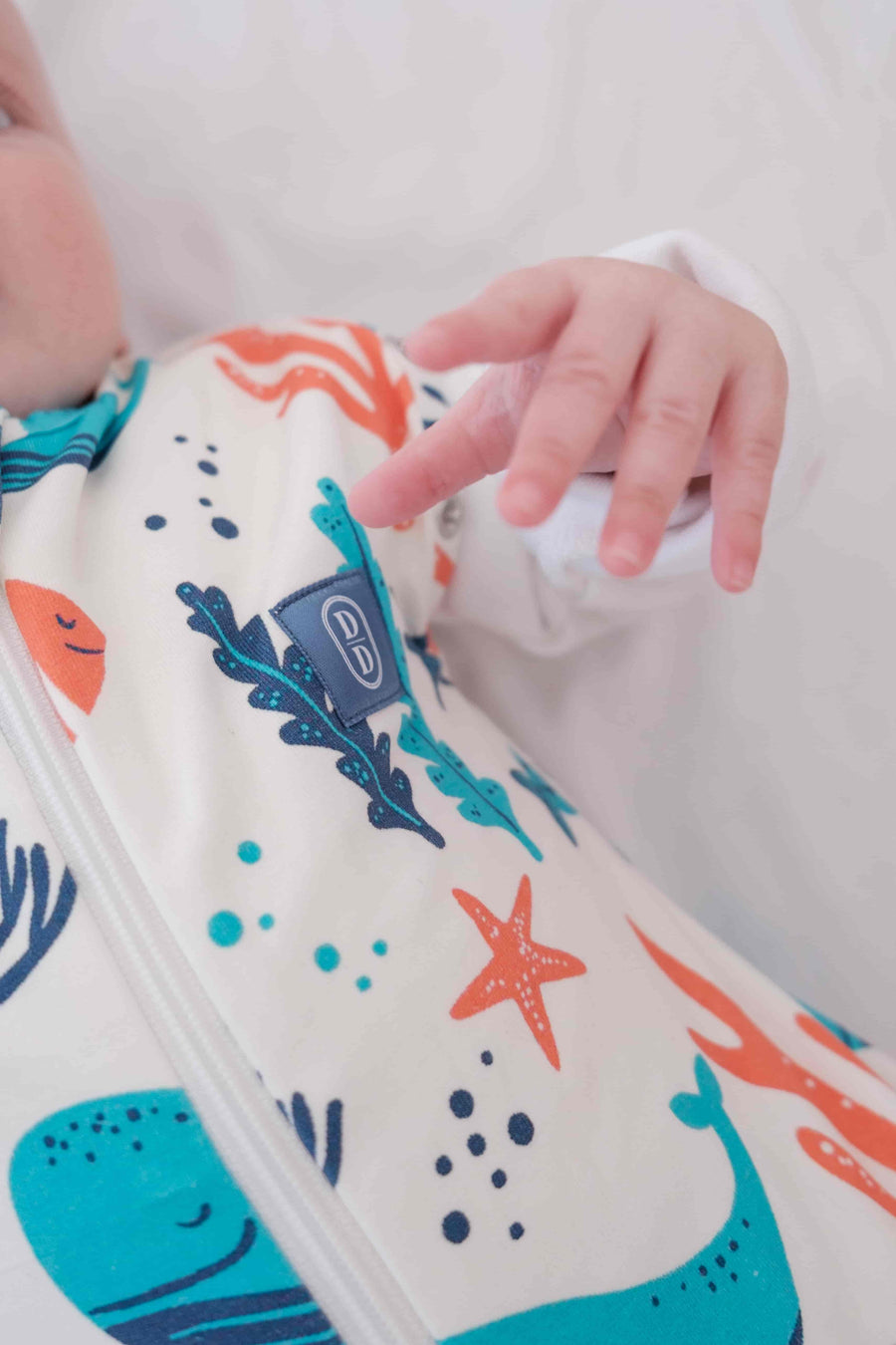 Newborn baby swaddled in a colourful dreamy days dream swaddle with ocean-themed design, lying on a white surface.